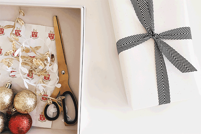 Holiday gifting: gift wrap, Christmas decorations and scissors beside a gift wrapped present.